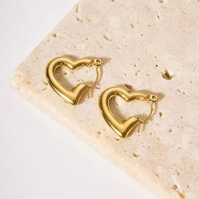Gold heart-shaped hoop earrings on a textured beige surface