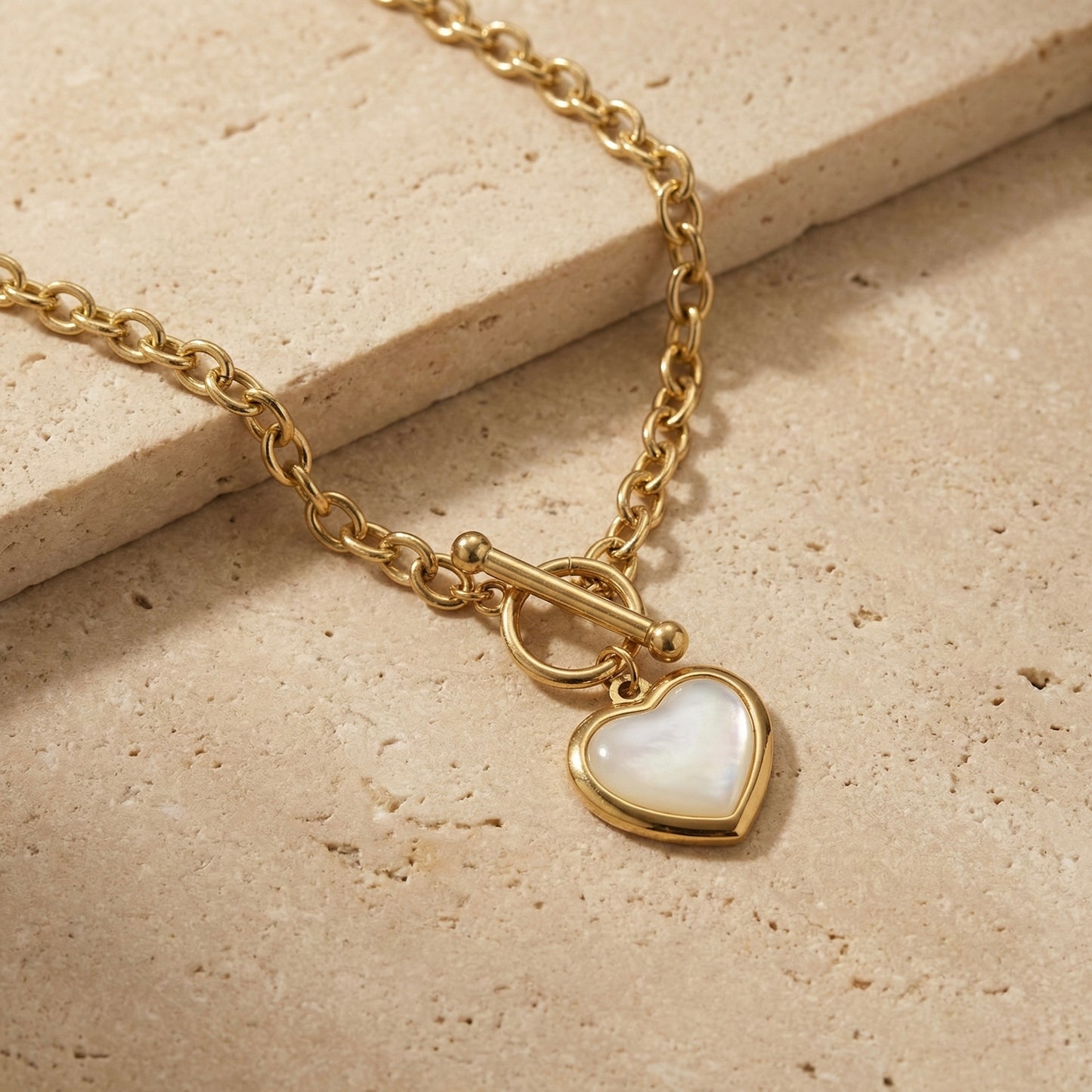 Gold necklace with a heart-shaped pendant on a beige stone surface