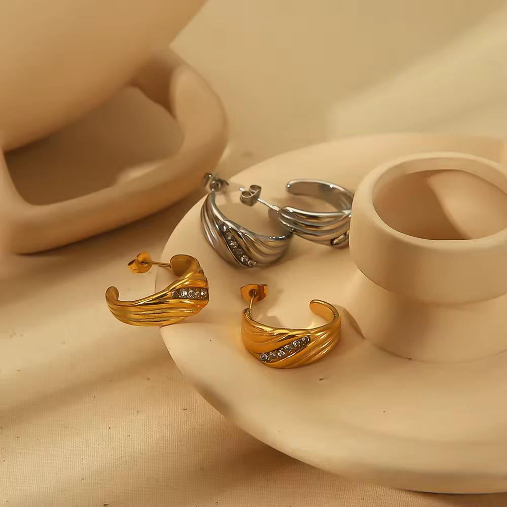 Gold and silver hoop earrings on a beige ceramic stand.