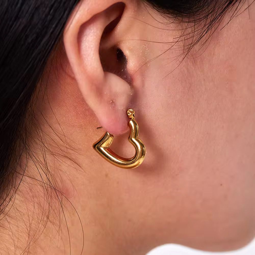 Gold open heart hoop earring worn by a person 