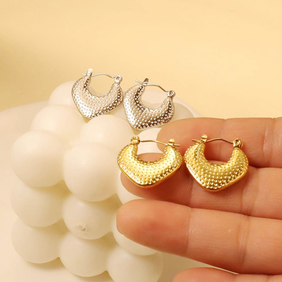 Gold and silver hoop earrings displayed on a hand with a beige background
