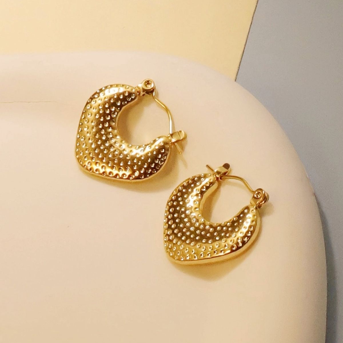 Gold hoop earrings on a light beige surface with a neutral background