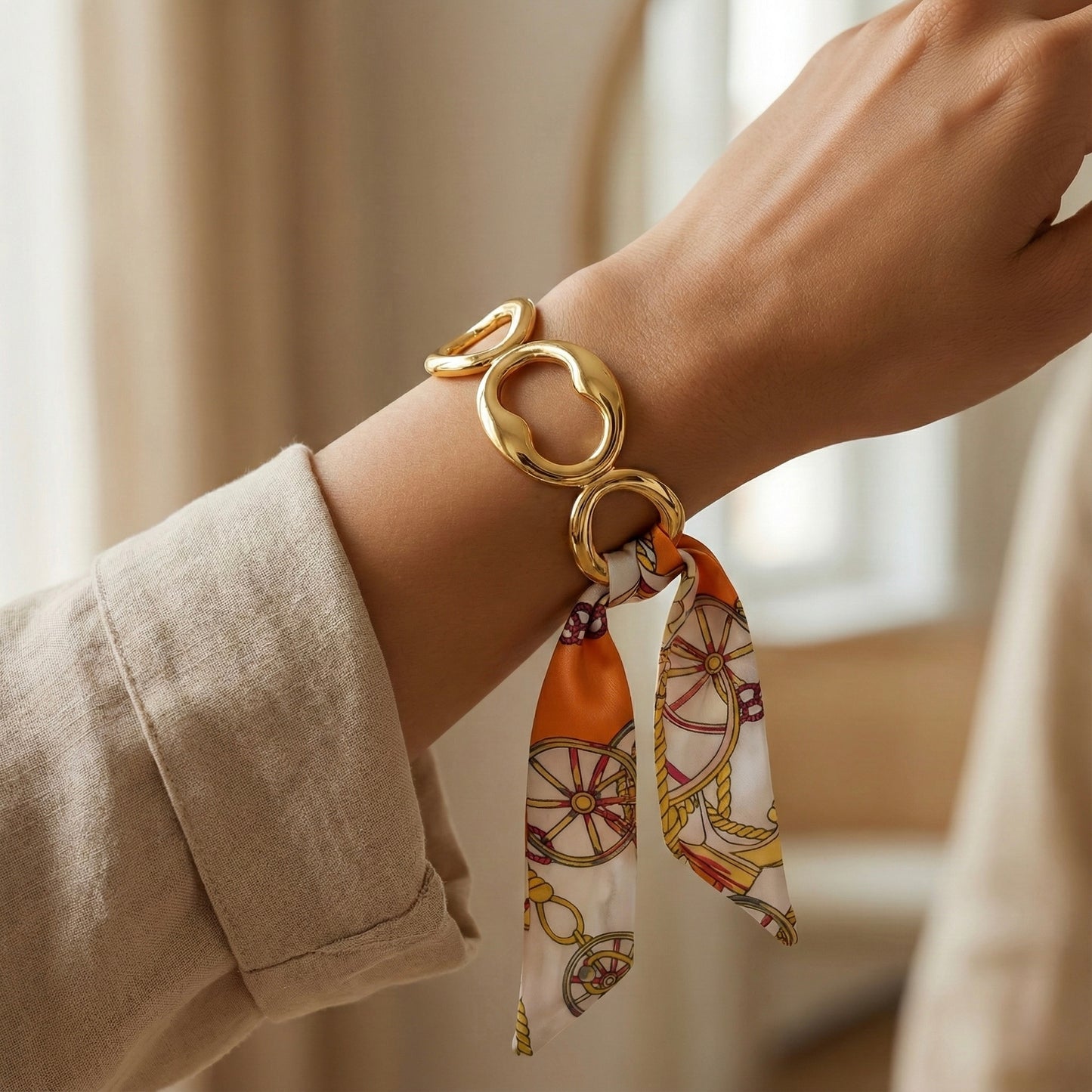 Gold bracelet with a patterned scarf on a wrist against a neutral background