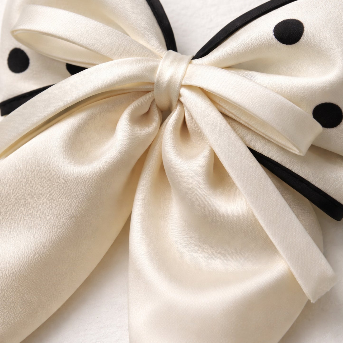 Close-up of a large cream-colored bow with black polka dots on a white background