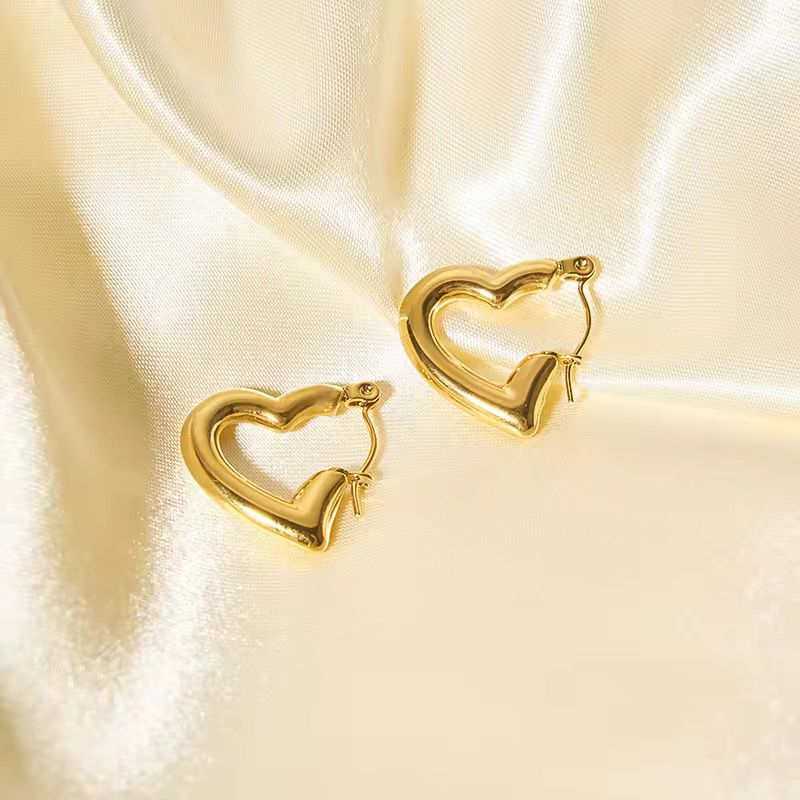 Gold heart-shaped hoop earrings on a satin surface